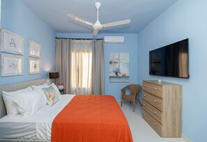 Ein Schlafzimmer mit einem Bett, einem Schminktisch, einem Stuhl, einem Deckenventilator, einem Fenster und einem Fernseher an der Wand.