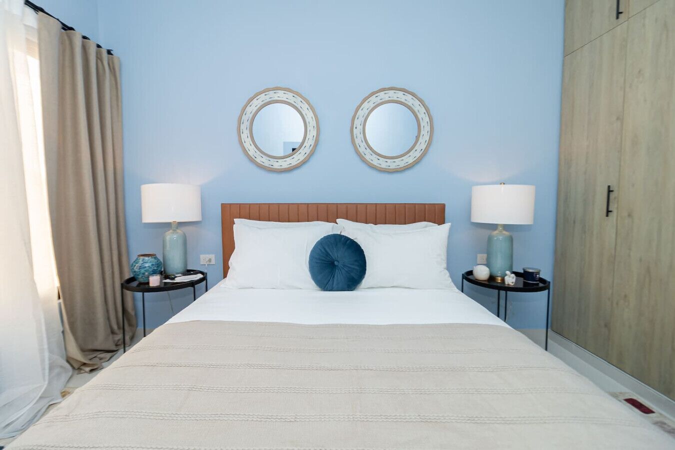 A neatly made bed with white linens and a blue accent pillow, flanked by two bedside tables with lamps and decorative items.
