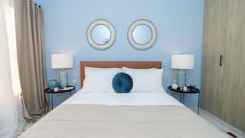A neatly made bed with white linens and a blue accent pillow, flanked by two bedside tables with lamps and decorative items.