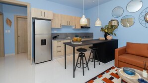 Une cuisine moderne équipée d’un réfrigérateur, de meubles en bois, d’un plan de travail noir et de deux tabourets de bar.