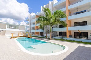 Un edificio moderno con piscina, palmeras y varios balcones.