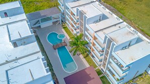 A modern multi-story hotel with a rooftop pool, balconies, and a landscaped area with palm trees.