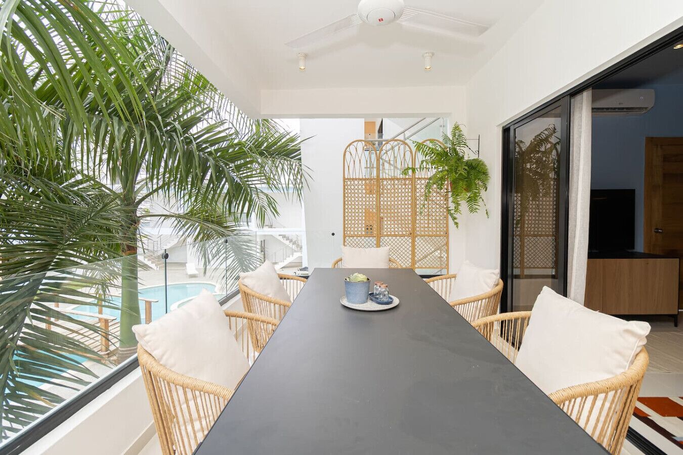 A modern dining area with a long table, wicker chairs, and a view of a pool.