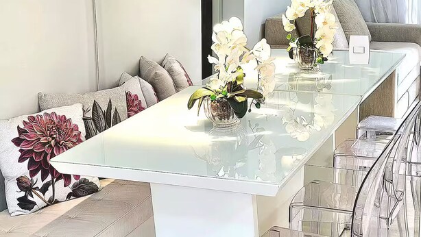 Zona d'esmorzar moderna amb taula de vidre, sofà blanc i cadires transparents.