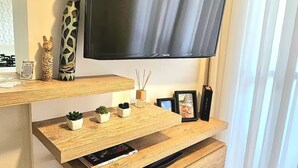 Un saló modern amb televisió de pantalla plana penjada a la paret, prestatges de fusta amb objectes decoratius i un moble de televisió integrat amb comandaments a distància.