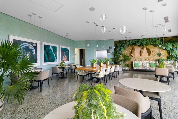 A spacious lobby with a green wall, multiple seating areas, and hanging spherical light fixtures.