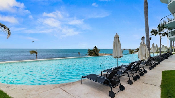 Zona junto a la piscina con sillones de descanso y sombrillas, con vista a un océano azul y cristalino.