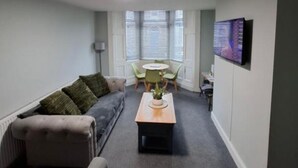 A living room with a sofa, a coffee table, a TV, and a dining area with chairs. - Stylish 4-Bed  with Sauna /Jacuzzi City Centre Location near Stadium of Light (Sunderland)