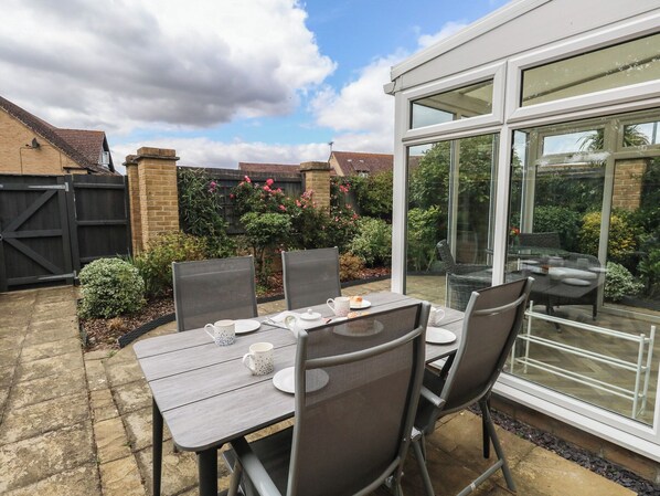 A patio area with a table set for two, surrounded by chairs, and a glass enclosure with a view of a garden. - June Cottage (Dorchester)