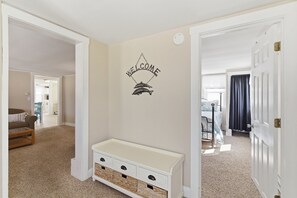 A hallway with a welcome sign, a bench, and a door leading to another room.