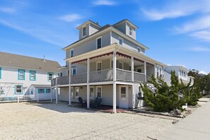 A two-story building with a balcony, a covered porch, and a gravel driveway. - Seaside Park 3BR Beach Retreat Ocean Block, Patio, Grill & Parking (Seaside Park)