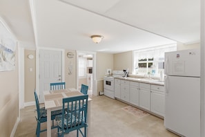 A kitchen with white cabinets, a dining table with chairs, a refrigerator, and a window with a view.