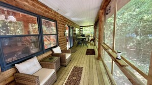 A log cabin with a porch, wicker furniture, and large windows overlooking a forest. - Welcoming 4-bedroom cabin in Chesterville (Chesterville)
