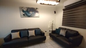 Una sala de estar con dos sofás oscuros, un árbol decorativo y un cuadro abstracto moderno en la pared.