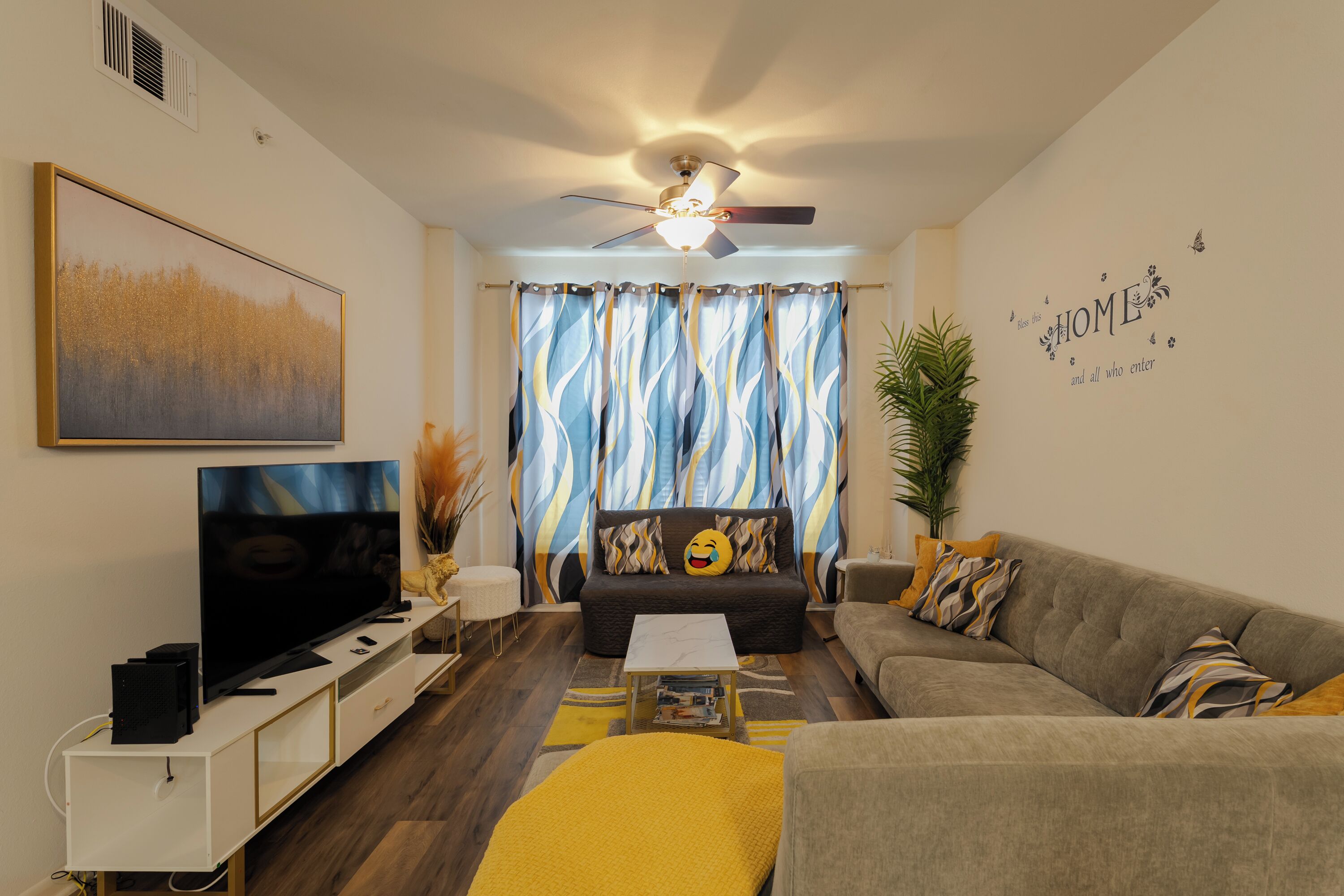 A living room with a flat-screen TV, a ceiling fan, and a sofa with decorative pillows.