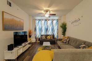A living room with a flat-screen TV, a ceiling fan, and a sofa with decorative pillows.