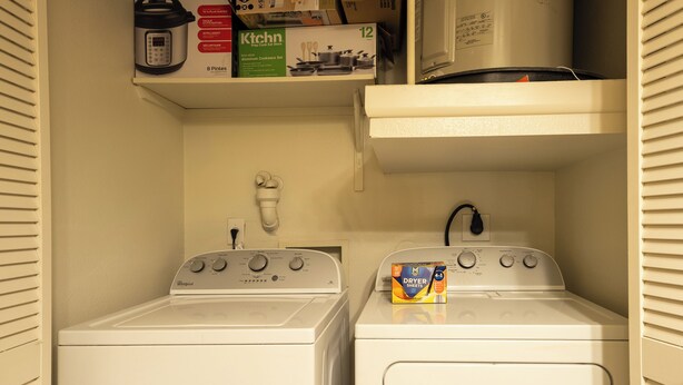 A laundry room with two front-loading washers, a microwave, and a shelf with kitchenware. - 1-bedroom apartment in The Domain with infinity pool+fitness room+2025 smart TV (Leander)