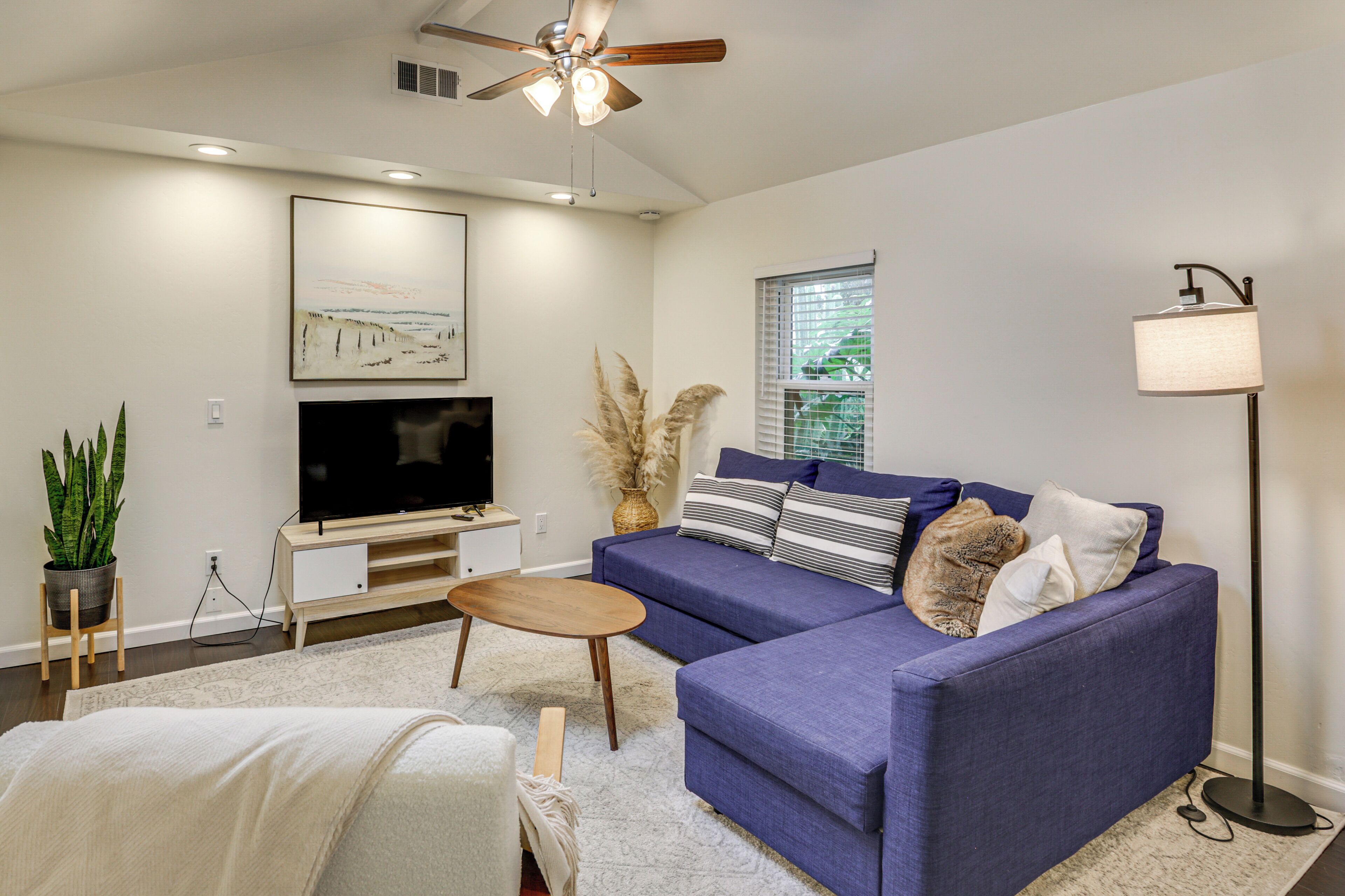 A modern living room with a blue sofa, a flat-screen TV, a ceiling fan, and a floor lamp.