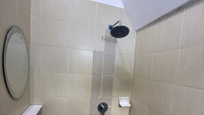 Ein Badezimmer mit beigen Fliesen, einer Duschbrause, einer Toilette und einem Spiegel.