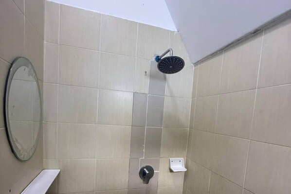 Un baño con baldosas color crema, un cabezal de ducha, un inodoro y un espejo.