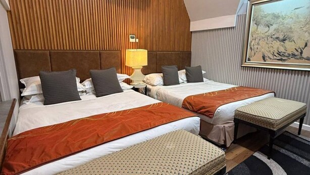 Ein Hotelzimmer mit zwei Betten, einem Holz-Kopfteil, einem Nachttisch mit Lampe und einem Bild an der Wand.
