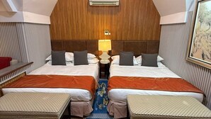 Ein Hotelzimmer mit zwei Betten, einer Holzbalkendecke, einem blauen Teppich mit Blumenmuster und einem kleinen Tisch mit einer Lampe.