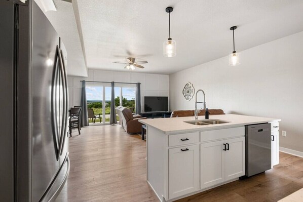 A modern kitchen with a central island, a built-in dishwasher, and a ceiling fan.