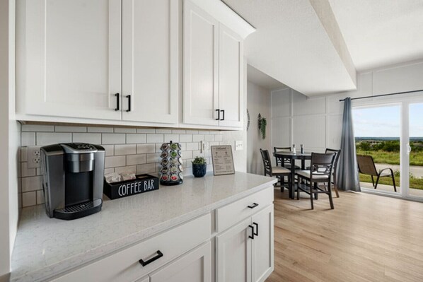 A modern kitchen with white cabinets, a coffee bar, and a dining area with a view.
