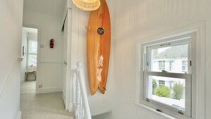 Una escalera con barandilla blanca, una tabla de surf montada en la pared y un ventanal con vista a una casa y follaje.