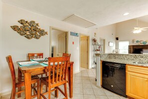 A dining area with a wooden table and chairs, a kitchen with a dishwasher and granite countertop, and a hallway with a door leading to another room. - Walk to East Beach: Apt w/ Outdoor Space (Norfolk)