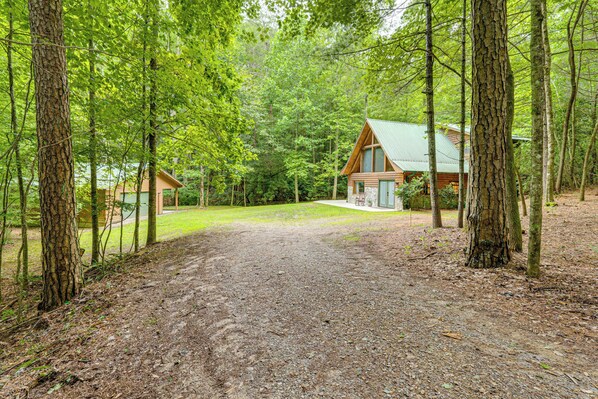 A cabin with a gravel driveway leading to a wooden deck, surrounded by dense forest. - Hike, Fish & More: Cozy Cabin w/ Patio in Murphy! (Murphy)