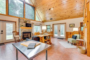 A spacious living room with a stone fireplace, wooden ceiling, and large windows. - Hike, Fish & More: Cozy Cabin w/ Patio in Murphy! (Murphy)