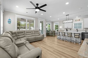 A modern kitchen with white cabinets, a dining area with a wooden table and chairs, a large L-shaped sofa, and a ceiling fan. - Luxury Beach House, Elevator, Golf Cart & Grill! (Myrtle Beach)