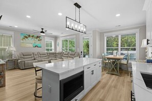 A modern kitchen with a central island, a dining area with a table and chairs, a sofa, and a ceiling fan.