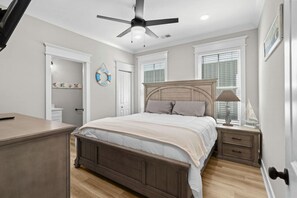 A bedroom with a bed, bedside table, nightstand, ceiling fan, and a door leading to another room. - Luxury Beach House, Elevator, Golf Cart & Grill! (Myrtle Beach)