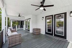 A covered porch with a ceiling fan, a seating area with a cushioned bench, and a large window with a view of the outdoors.