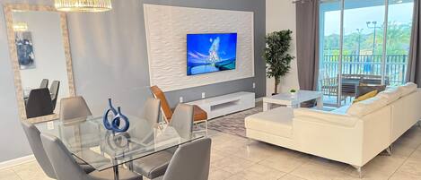 Una sala de estar moderna con un televisor de pantalla plana, una mesa de comedor de vidrio y un sofá blanco.