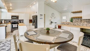 A modern kitchen with white cabinetry, a central island with seating, a ceiling fan, and a stone backsplash. - Welcoming Group Getaway w/ Pool & Patio in Peoria! (Peoria)