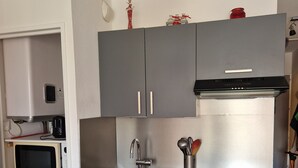 A compact kitchen with grey cabinets, a stainless steel sink, a microwave, and a refrigerator with magnets.