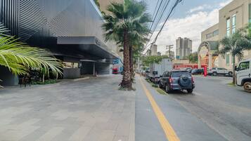 A modern building with a geometric facade, a palm tree, and parked vehicles on a city street.
