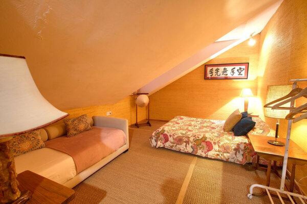 A cozy attic room with a sofa, a bed with floral bedding, a lamp, and a wooden desk.