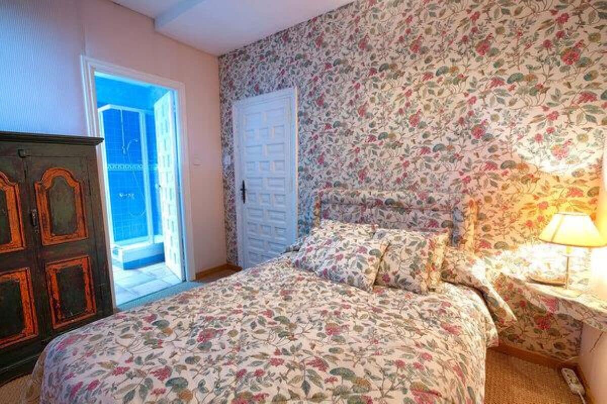 A bedroom with a floral-patterned bedspread, a wooden wardrobe, and a door leading to an outdoor area.