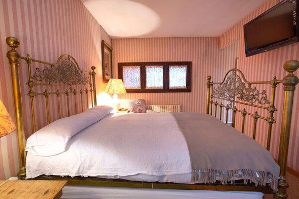A bedroom with a large bed, striped wallpaper, a window, and a television on the wall.