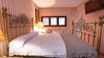 A bedroom with a large bed, striped wallpaper, a window, and a television on the wall.