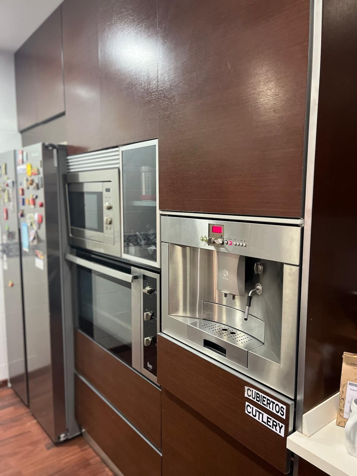 A kitchen with stainless steel appliances, including a microwave and a coffee machine, and a sign indicating a cutlery station.