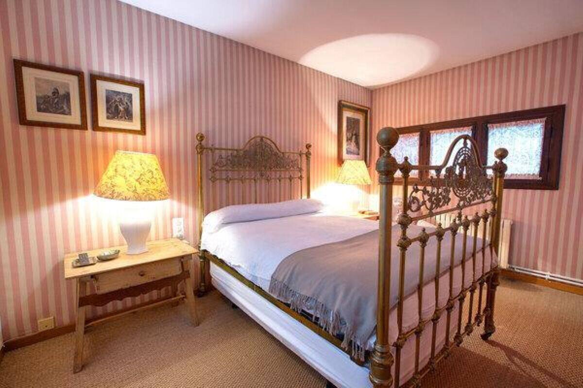 A bedroom with a single bed, two bedside lamps, a wooden nightstand, and a window with a view.