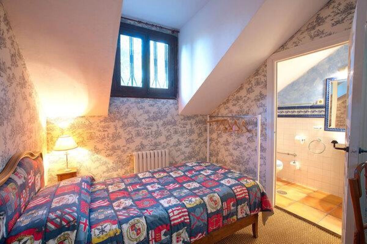 Une chambre à coucher avec un lit, une fenêtre et une salle de bain visible à travers une porte ouverte.