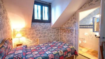Une chambre à coucher avec un lit, une fenêtre et une salle de bain visible à travers une porte ouverte.