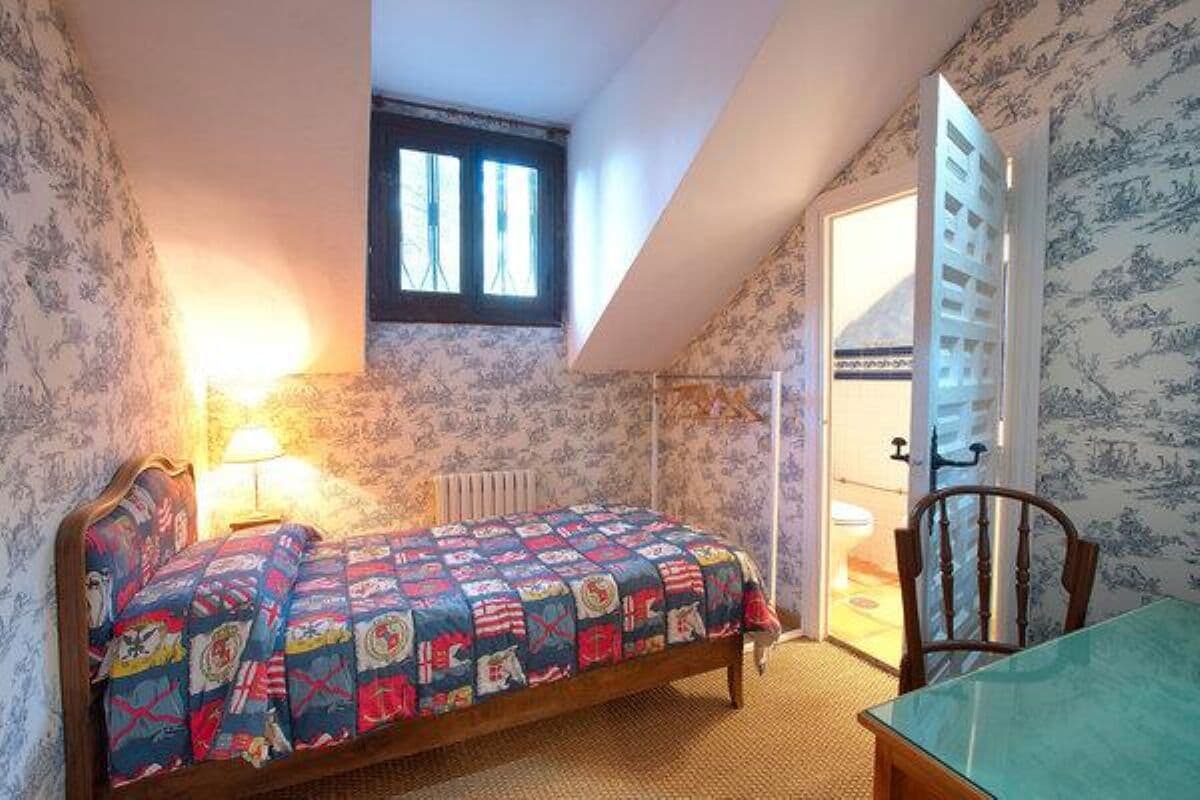 Un dormitorio con cama, una silla, una mesa, una ventana y una puerta.