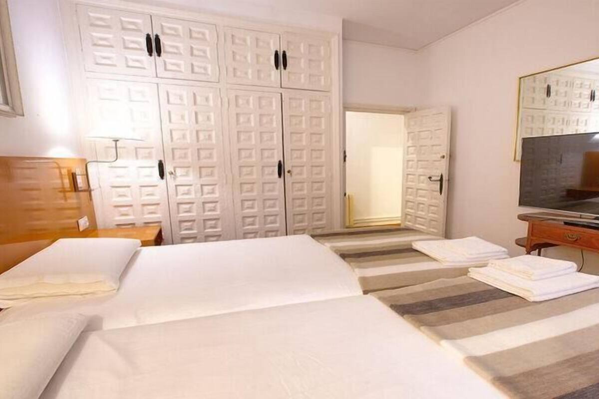 A hotel room with two beds, a TV, a wooden dresser, and a large wardrobe.